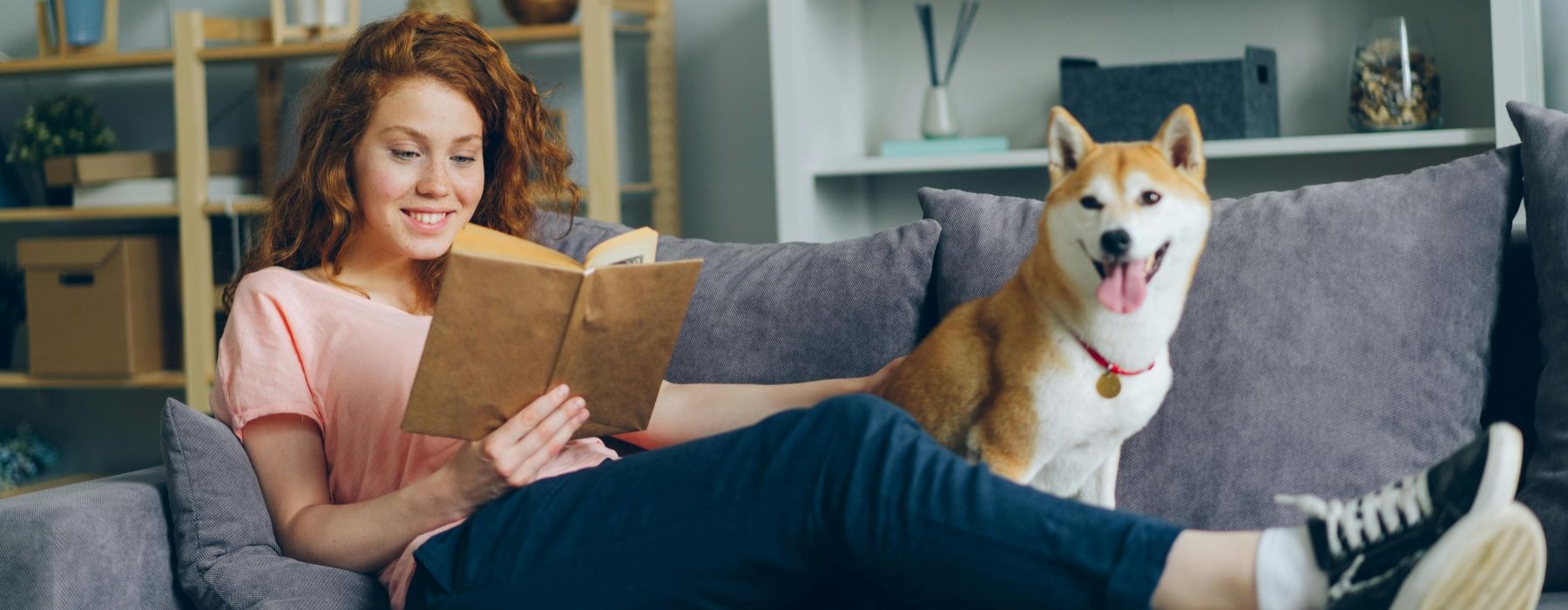 Woman reading a book on a couch with her dog sitting next to her